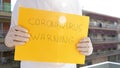 Sign with text `CORONAVIRUS WARNING` in hands with surgical gloves.