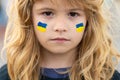 Sign of ukrainian flag on child cheek. Ukrainian geopolitics globe crisis. Close up kids face.