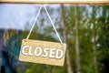 Rustic wooden Closed sign on rope hanging on glass business door reflecting pine forest - close-up and room for copy Royalty Free Stock Photo