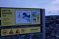 A Sign Which Informs About The Dangers On Reynisfjara Beach, With Smashing Waves In The Background
