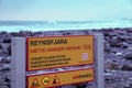 A Sign Which Informs About The Dangers On Reynisfjara Beach, With Smashing Waves In The Background