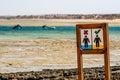 Sign in a Wooden Frame on the Beach Near the Egyptian Red Sea Prohibiting Walking on Corals with Two Boats in the Backround Royalty Free Stock Photo