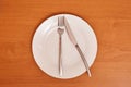 Empty and clean white plate with fork and knife on a wooden table as an example of table etiquet