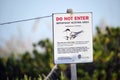 Signboard with warning about nesting area of sea birds on seaside beach with small sand dunes and grassy vegetation on