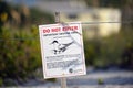 Signboard with warning about nesting area of sea birds on seaside beach with small sand dunes and grassy vegetation on