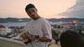 Signing man relax balcony on weekend holiday. Carefree guy play ukulele guitar