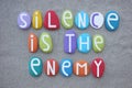 Silence is the enemy, creative slogan composed with multi colored stone letters over beach sand
