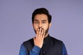 Silence or mistake concept. Shocked Indian man covering mouth with his hand over lilac background