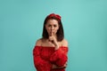 Silence please. European woman, brunette in red dress with bare shoulders wearing hair band keeps fore finger over lips Royalty Free Stock Photo