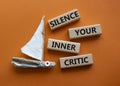 Silence your inner critic symbol. Wooden blocks with words Silence your inner critic. Beautiful orange background with boat.