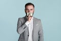 Silenced by money. Young businessman covering his mouth with hundred dollar bill over blue background