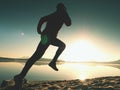 Silhouette of active athlete runner running on sunrise shore. Morning healthy lifestyle exercise