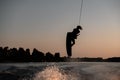 silhouette of active male rider holds rope and making extreme jump on wakeboard at sunset.