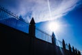 Silhouette against the sun of a high wall and metal fence with an intense blue sky in the background Royalty Free Stock Photo