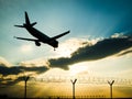 Silhouette of airplane landing in sunset to the airport behind barbed wire fence Royalty Free Stock Photo