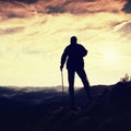 Silhouette of alone hiker with poles in hand. Tourist with sporty backpack stand on rocky view point above misty valley. Sunny spr Royalty Free Stock Photo