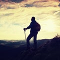 Silhouette of alone hiker with poles in hand. Tourist with sporty backpack stand on rocky view point above misty valley. Sunny spr