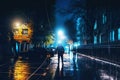 Silhouette of alone stranger in hood at night city street in rain. Creepy killer or stalker, criminal stands in shadow