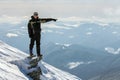 Silhouette of alone tourist standing on snowy mountain top in winner pose with raised hands enjoying view and achievement on Royalty Free Stock Photo