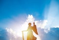 Silhouette of angel statue sculpture with sunlight shining behind white cloud with blue sky background.