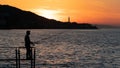 Silhouette of an angler man. Man fishing at sunset by the sea. Man and city silhouette. Selective focus included