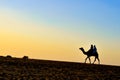 Silhouette of an Arabian camel carrying tourists in Sam Sand Dunes, Thar Desert, Jaisalmer, India. These sand dunes are amongst