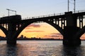 Silhouette of arched railway bridge and a train at beautiful sunset. Dnieper river, Dnipo city, Ukraine.