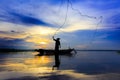 Silhouette asian fisherman on wooden boat casting a net for catching freshwater fish in nature river in the early morning
