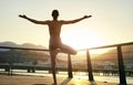 silhouette athletic woman standing on bridge with open arms in Tree Yoga Pose during sunset