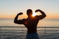 Silhouette of athletic young man showing biceps at sunnrise