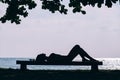 Silhouette of attractive woman in bikini lying on the bench near the sea