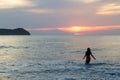 Silhouette back view of young woman in bikini entering into the Pacific Ocean during a pink sunset Royalty Free Stock Photo