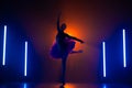 Silhouette of ballerina is practicing elements in studio with neon colorful light. Young woman dancing in classic tutu