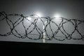 silhouette of barbed wire on a fence against a background of blurry lamp posts at foggy night Royalty Free Stock Photo