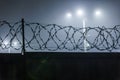 silhouette of barbed wire on a fence against a background of blurry lamp posts at foggy night Royalty Free Stock Photo