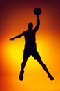 Silhouette of basketball player in motion, action on gradient yellow orange background in neon light. Sport, diversity,