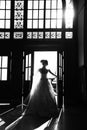 Silhouette of a beautiful bride in a traditional white wedding dress, stood by window.