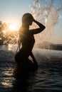 Silhouette of beautiful brunette woman in swimsuit posing in outdoor pool over sunset sky Royalty Free Stock Photo