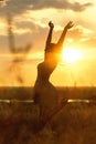 Silhouette of a beautiful girl dancind and spinning in a dress at sunset in a field, happy young woman enjoying nature