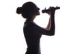 Silhouette of beautiful girl with hand-picked hair singing into microphone, profile of young woman face performing lyric song on