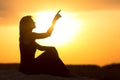 Silhouette of beautiful girl sitting on the sand and enjoying the sunset, the figure of young woman on the beach showing up with