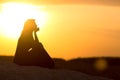 Silhouette of beautiful thoughtful girl sitting on the sand and enjoying the sunset, the figure of young woman on the beach, Royalty Free Stock Photo