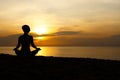 Silhouette of beautiful woman sitting cross legged in easy seat pose on the beach with sunrise in background Royalty Free Stock Photo