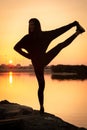 Silhouette of a beautiful yoga woman doing balance exercise at sunrise or sunset near the sea coast. Royalty Free Stock Photo