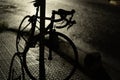 Silhouette of a bicycle leaning on a metal post on the side of a street