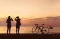 Silhouette bicycle and people take photo at beach sunset backgro