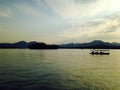 A silhouette boat and man sailing on the calm sea at sunset in the background of mountains and sun beams. Royalty Free Stock Photo