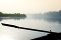 Silhouette of boat oar coming out of water with a foggy river in the background