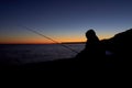 Silhouette of boy with fishing rod at calm sunset fishing off the cliff  long exposure photo Royalty Free Stock Photo