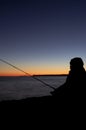 Silhouette of boy with fishing rod at calm sunset fishing off the cliff long exposure photo Royalty Free Stock Photo